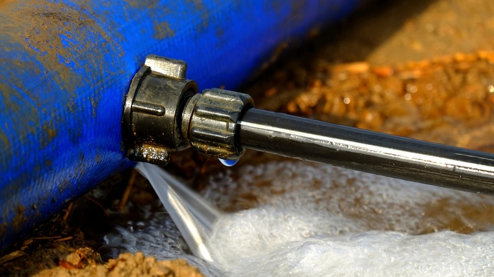 Wasser tritt an der Verschraubung einer blauen Leitung aus und schäumt am Boden auf